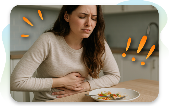 Woman holding her stomach at a table with a plate of food, representing food intolerance symptoms after eating.