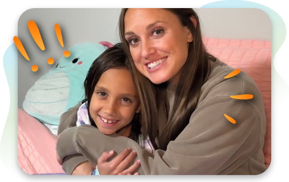 Woman smiling while hugging a young child on a couch in a cozy home setting.