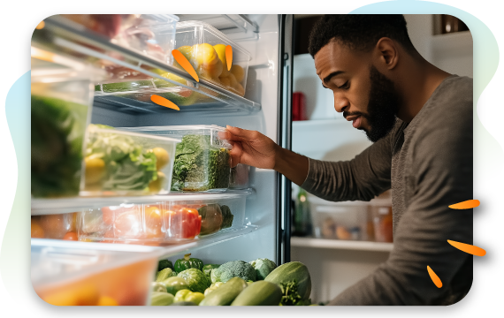 A man looks into an open refrigerator, filled with fresh vegetables and fruits in clear containers, as he reaches for a container of leafy greens. The image illustrates making a healthy food choice.